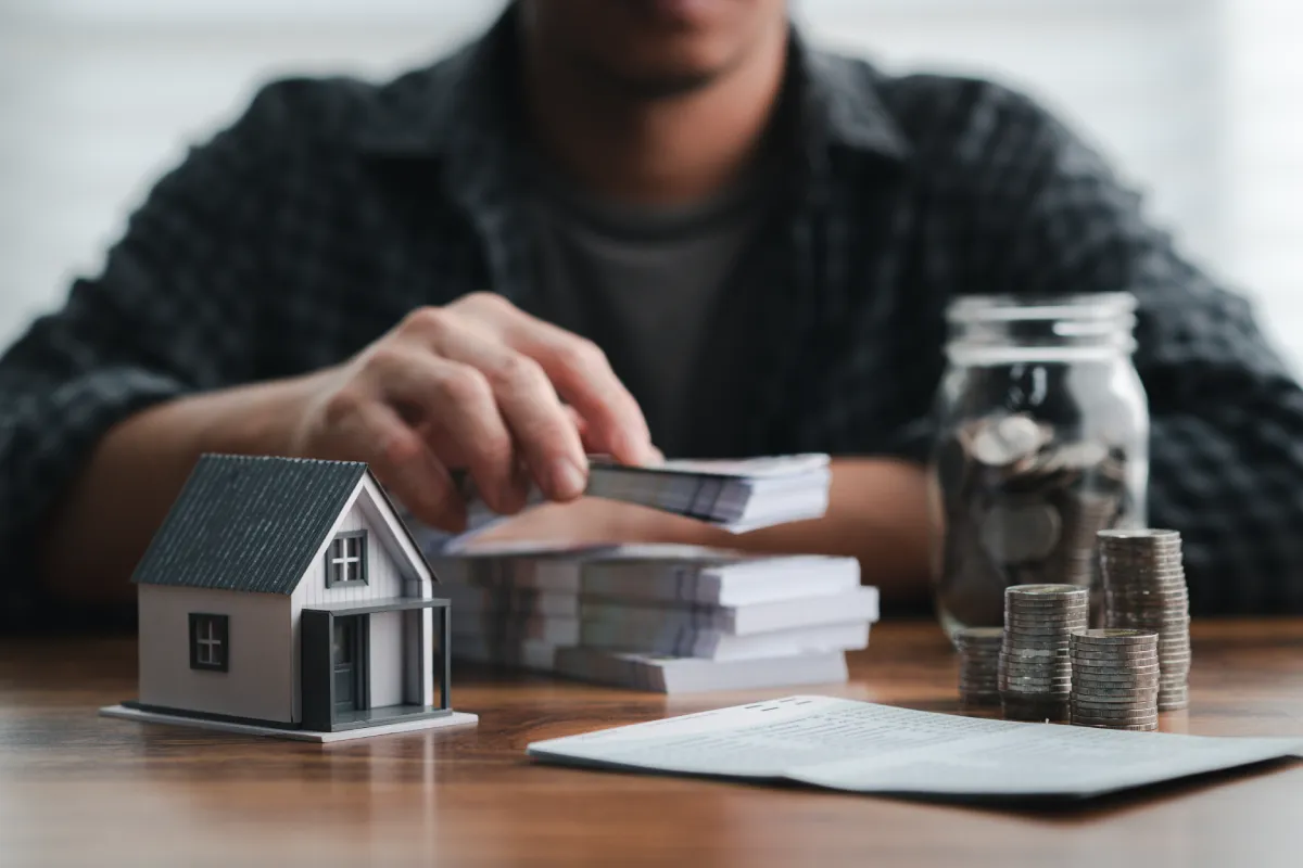 stół z małym domkiem, pieniędzmi i mężczyzna w tle